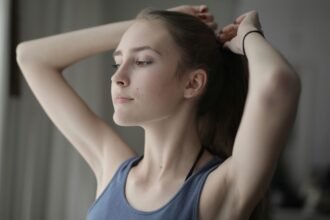 A focused young woman tying her hair and looking out a bright window, representing a fresh mental reset after a weekend dopamine detox.