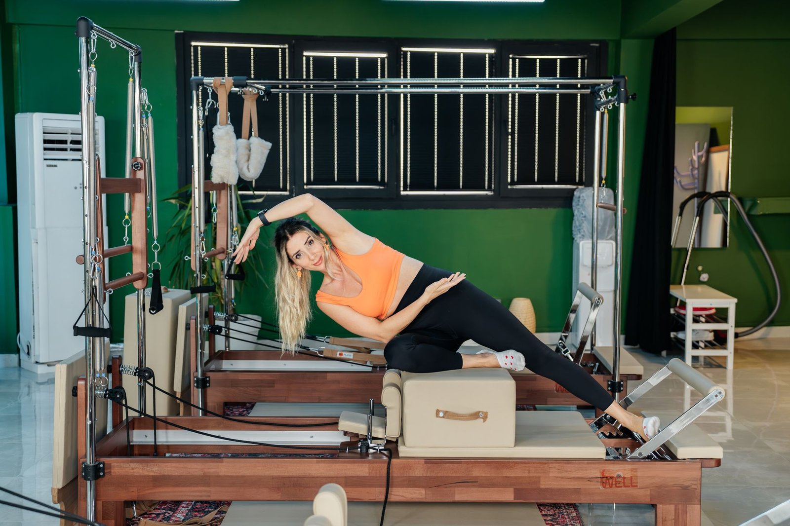 Senior woman performing wall-supported Pilates exercises in a bright living room.