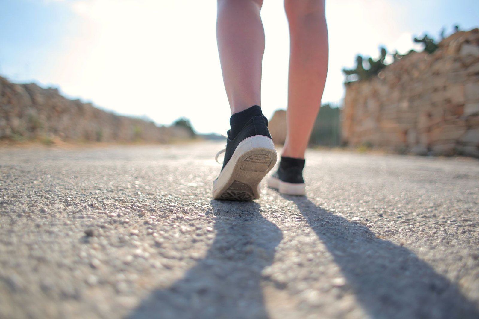 Person walking on a paved pathway during the golden hour of sunset.