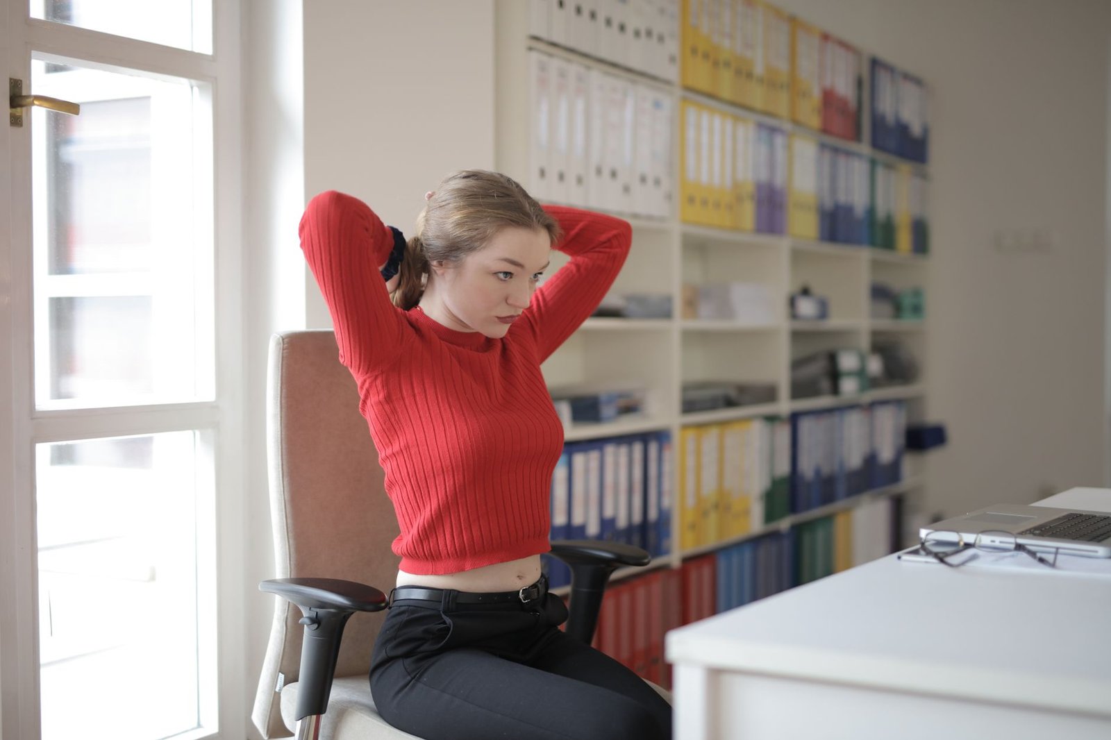 Woman performing a gentle neck stretch while standing in a bright room.