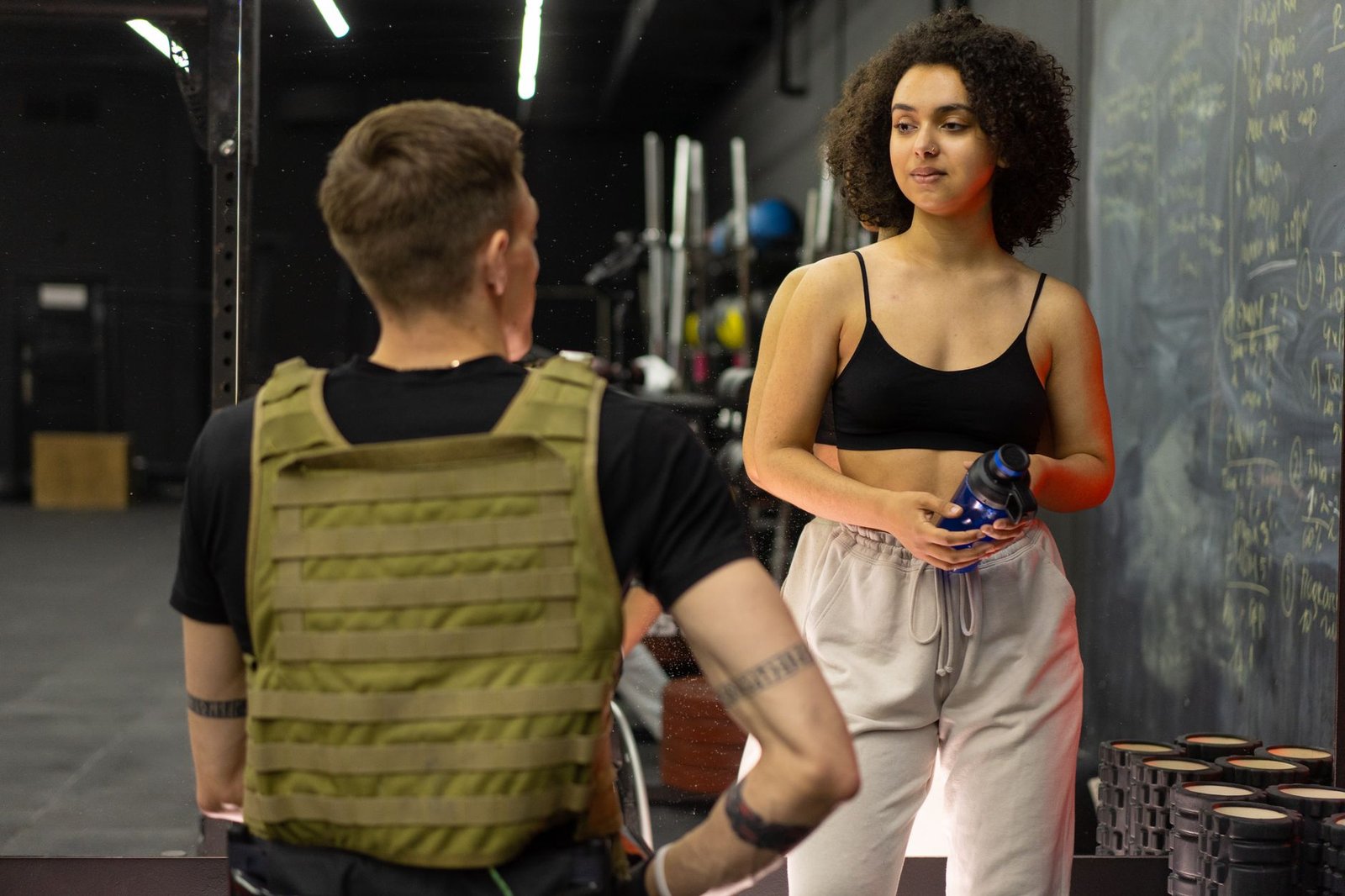Professional fitness coach guiding client on barbell lift in bright gym.