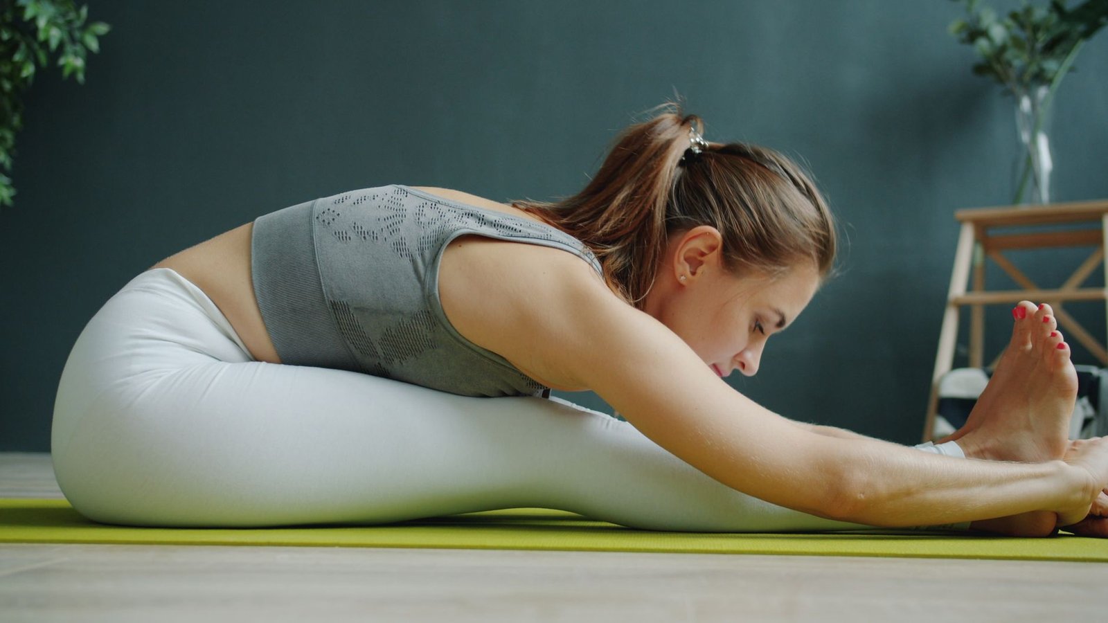 Woman performing a gentle hamstring and hip stretch in a home workout setting.