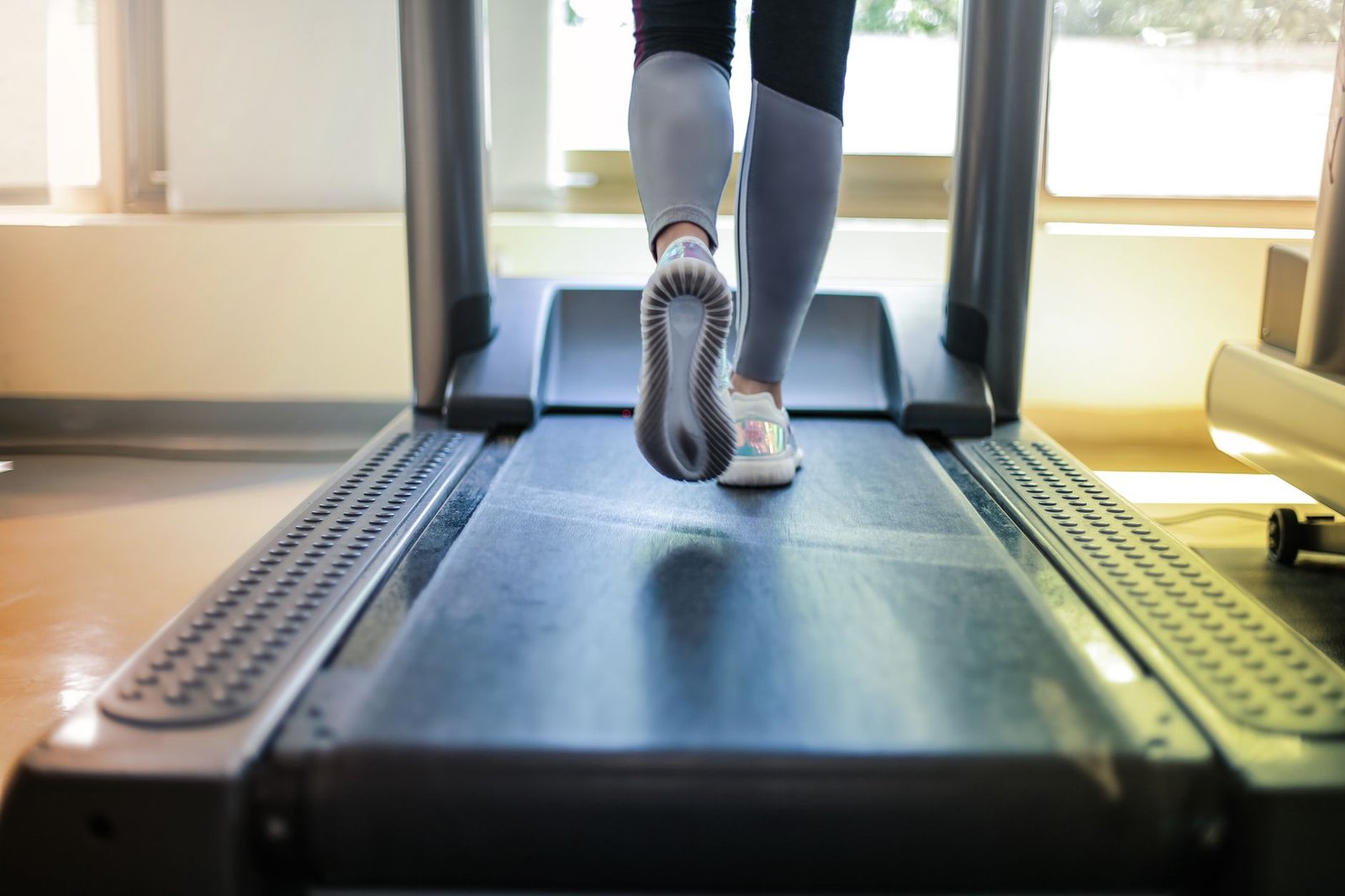 Proper cushioned athletic footwear aligned on an active low impact walking pad belt.